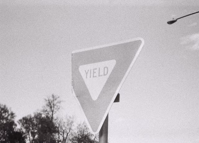 A yield sign with a bent corner, in black and white