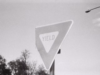 A yield sign with a bent corner, in black and white
