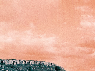 A blurry blue hill under a grainy orange sky, taken in portrait