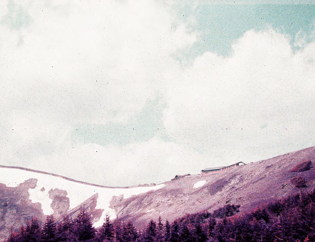A distant building on a purple hill under a green, partly-cloudy sky